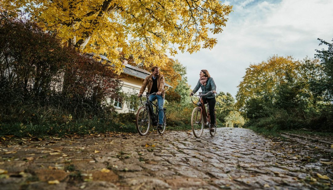 Zwei Personen fahren mit dem Fahrrad im Herbst auf Kopfsteinpflaster beim Gut Pohnstorf.