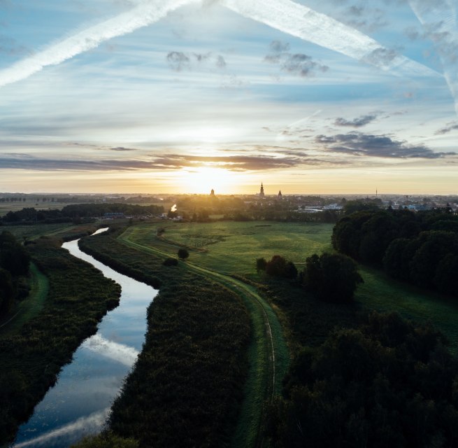 Sonnenaufgang über der Hansestadt Greifswald: Ein stiller Fluss schlängelt sich durch Wiesen, während Kirchtürme am Horizont langsam im Morgenlicht sichtbar werden. Mecklenburg-Vorpommern erwacht leise. // © MV-T/Gänsicke Sonnenaufgang über der Hansestadt Greifswald: Ein stiller Fluss schlängelt sich durch Wiesen, während Kirchtürme am Horizont langsam im Morgenlicht sichtbar werden. Mecklenburg-Vorpommern erwacht leise. // © MV-T/Gänsicke