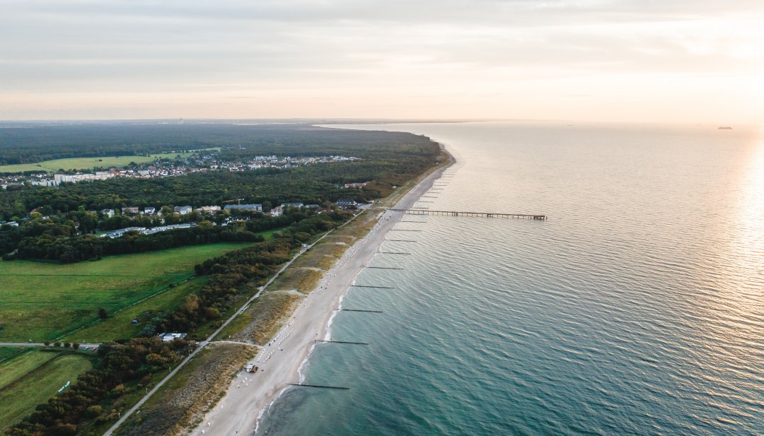 Luftaufnahme der Seebrücke und des Strandes von Graal-Müritz, umgeben von Wald und Wiesen, mit der Ostsee im Licht eines stimmungsvollen Sonnenuntergangs. // Die Seebrücke und der weite Sandstrand von Graal-Müritz im sanften Licht der Abendsonne: Ein idyllischer Ort, um die Schönheit der Ostseeküste zu genießen. // © MV-T/Gross Luftaufnahme der Seebrücke und des Strandes von Graal-Müritz, umgeben von Wald und Wiesen, mit der Ostsee im Licht eines stimmungsvollen Sonnenuntergangs.