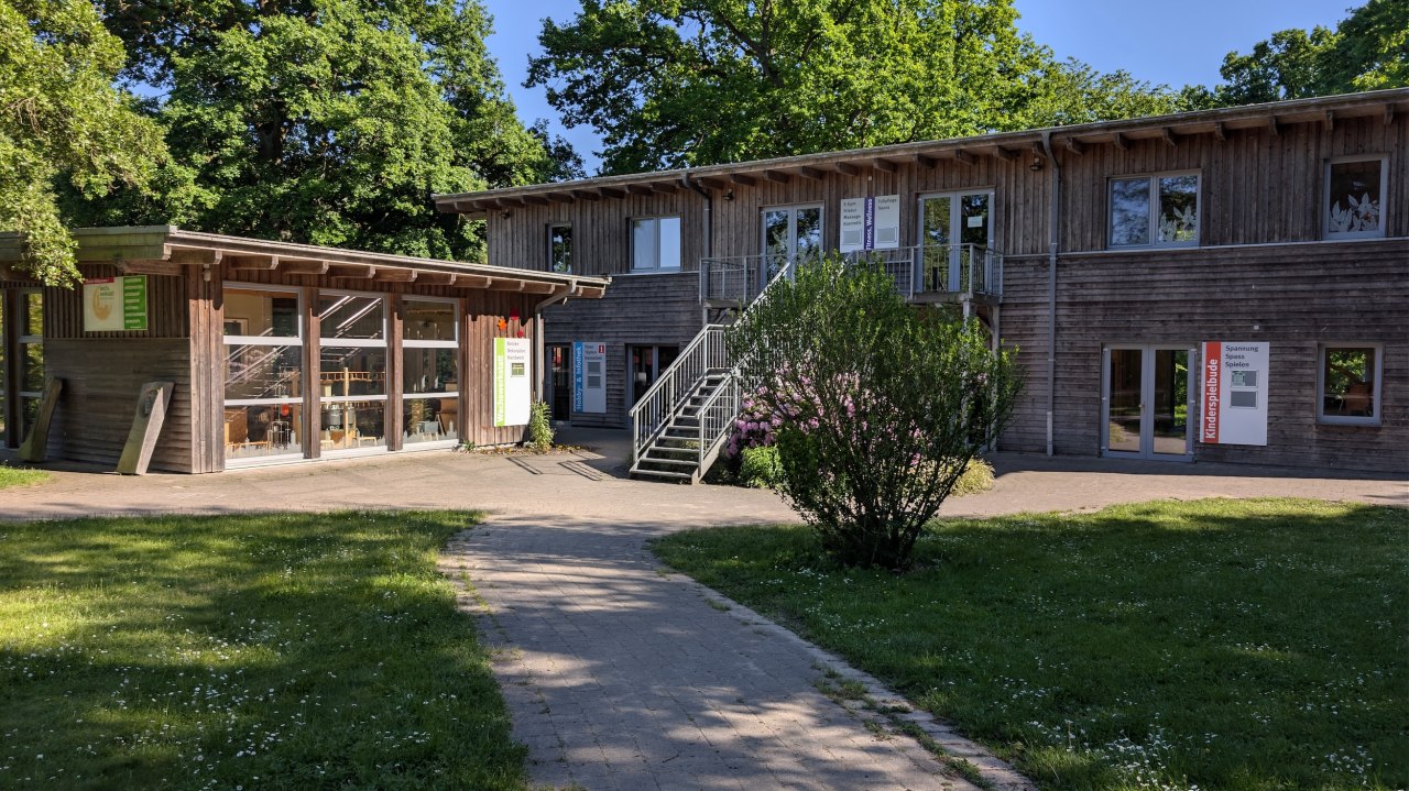 Het creatieve centrum vormt het hart van onze camping. Het gebouwencomplex herbergt op twee verdiepingen onze kaarsenmakerij, een pottenbakkerij, een yogaruimte, de speelhal, een fitnessruimte en een sauna. Voor het gebouw ligt een klein plein met veel groen, waar we graag verschillende feesten organiseren en waar ook onze mobiele boerderijwinkeltjes stoppen om regionale producten aan onze gasten te verkopen. // &copy; Carla Pommerehne / Campingplatz Seehof GmbH
