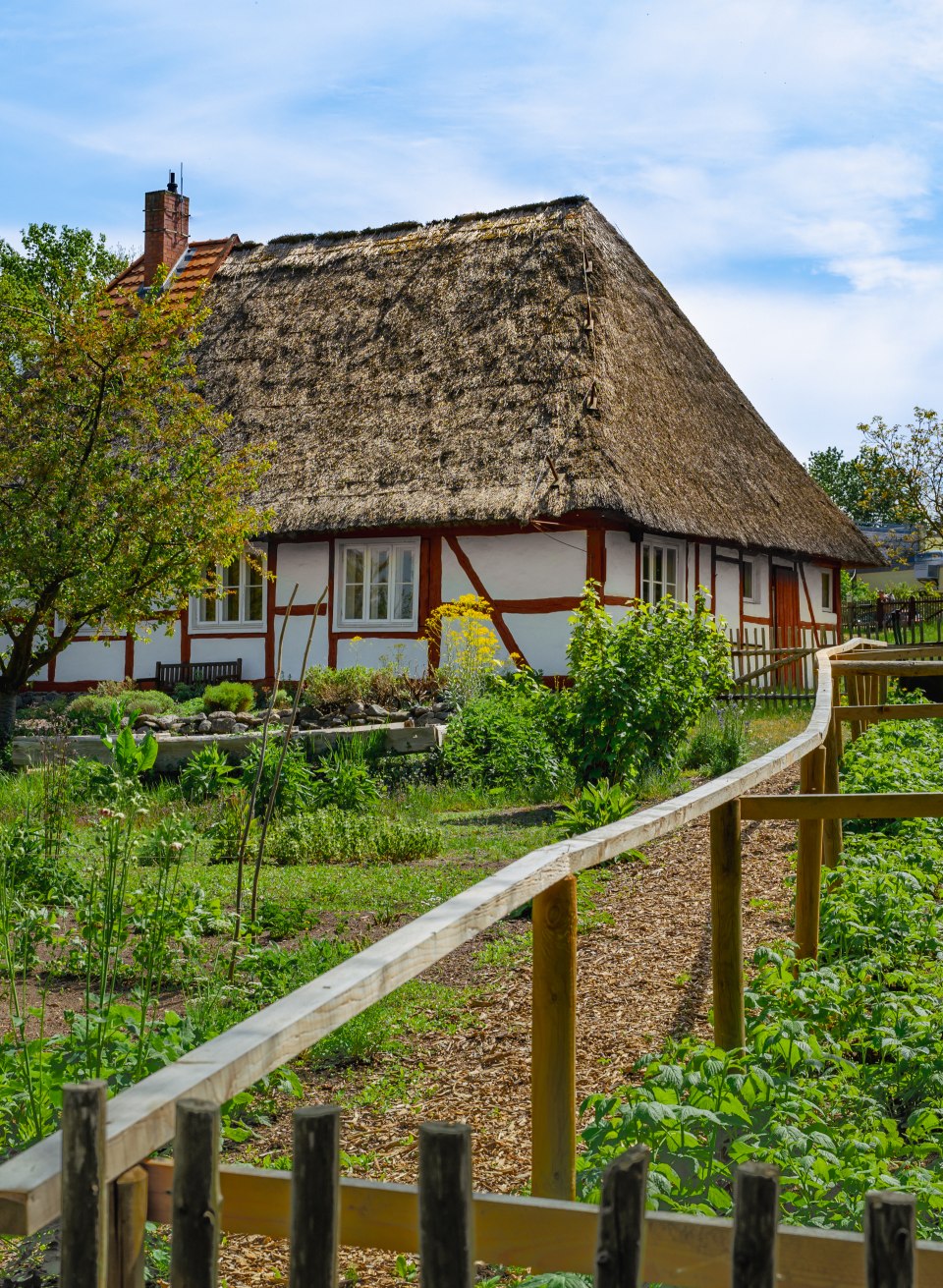 De tuin van de dorpsonderwijzer in het openluchtmuseum Mue&szlig; met een vakwerkhuisje met rieten dak.