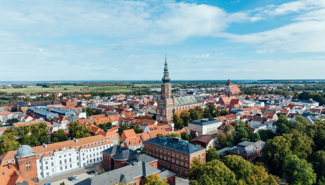 Die Silhouette von Greifswald aus der Luft und Blick auf die Kirchtürme, sowie Altstadt am Tage.