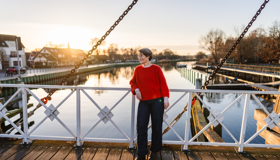 Frau auf der wei&szlig;en Wiecker Klappbr&uuml;cke bei Sonnenuntergang, im Hintergrund spiegelt sich der Ryck in Greifswald.