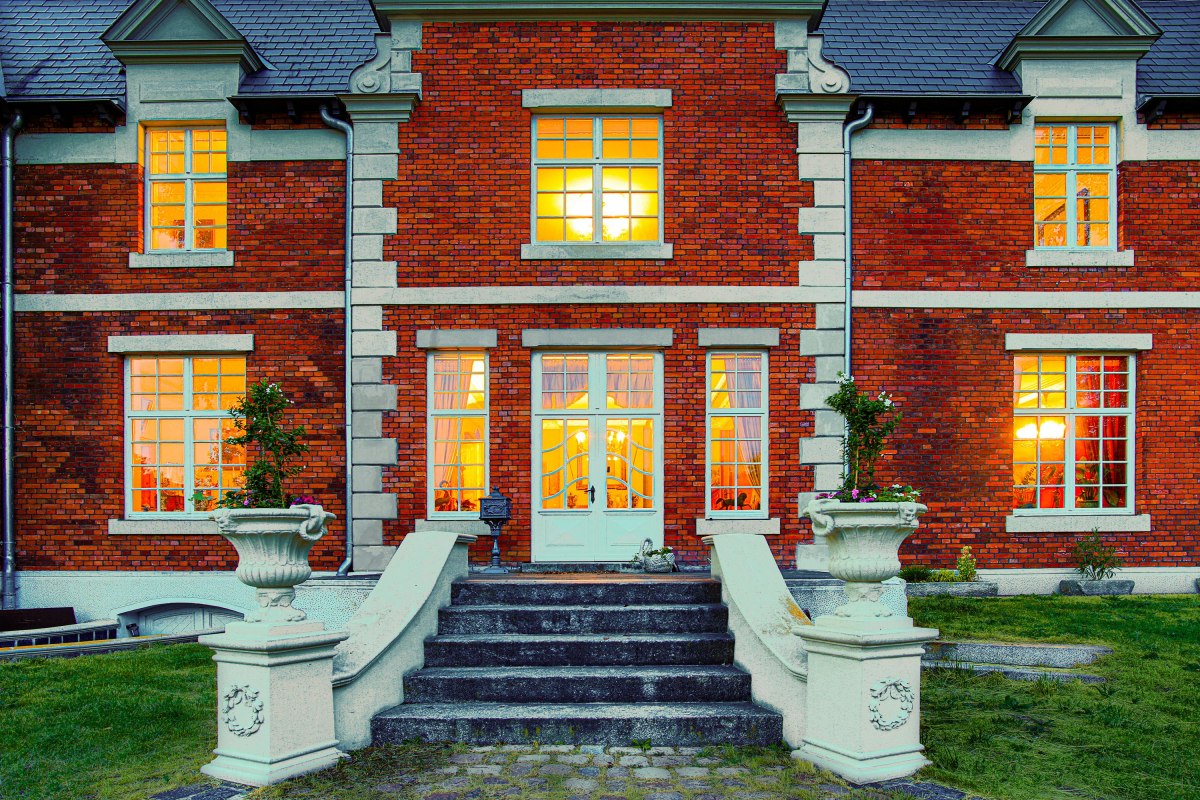 Illuminierter Eingang des Herrenhauses Brookhusen: Historistische Backsteinfassade und einladend leuchtende Fenster in der Abenddämmerung. // © Herrenhaus Brockhusen Illuminierter Eingang des Herrenhauses Brookhusen: Historistische Backsteinfassade und einladend leuchtende Fenster in der Abenddämmerung. // © Herrenhaus Brockhusen