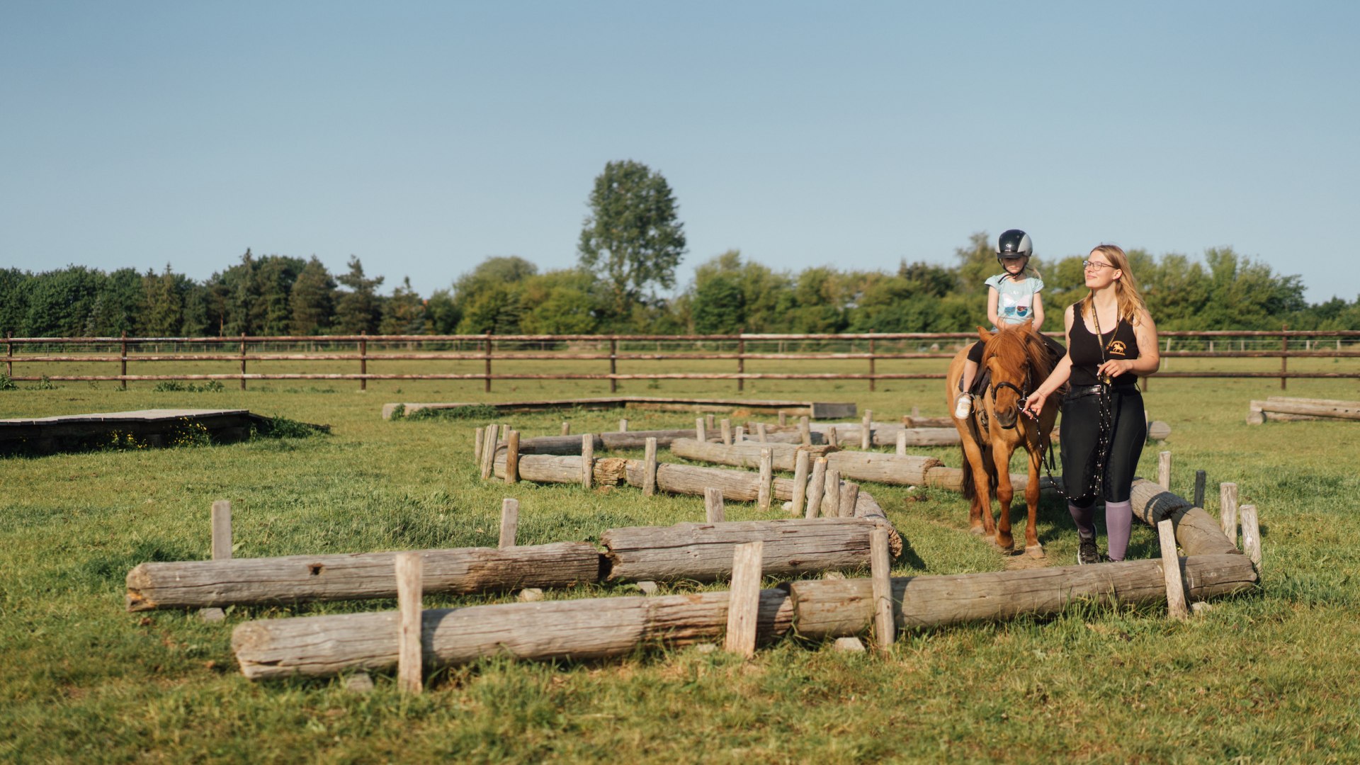 Ein Kind sitz auf einem Pony und wird von einer Reitlehrerin geführt.