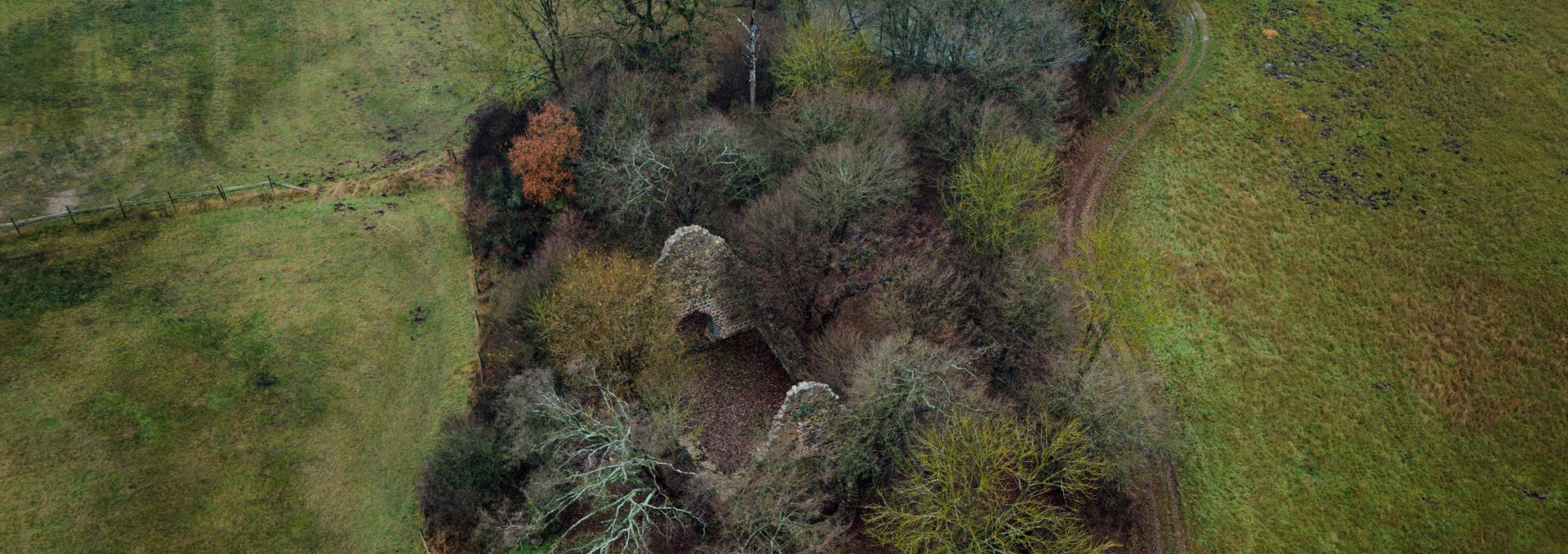 Historisches Kleinod im Grünen – Die Ruine der „Wüsten Kirche“ bei Ulrichshusen aus der Vogelperspektive, eingebettet in die sanfte Hügellandschaft., © TMV/Petermann Luftaufnahme der Ruine „Wüste Kirche“ bei Penzlin, umgeben von Bäumen, Wiesen und einem geschwungenen Weg.