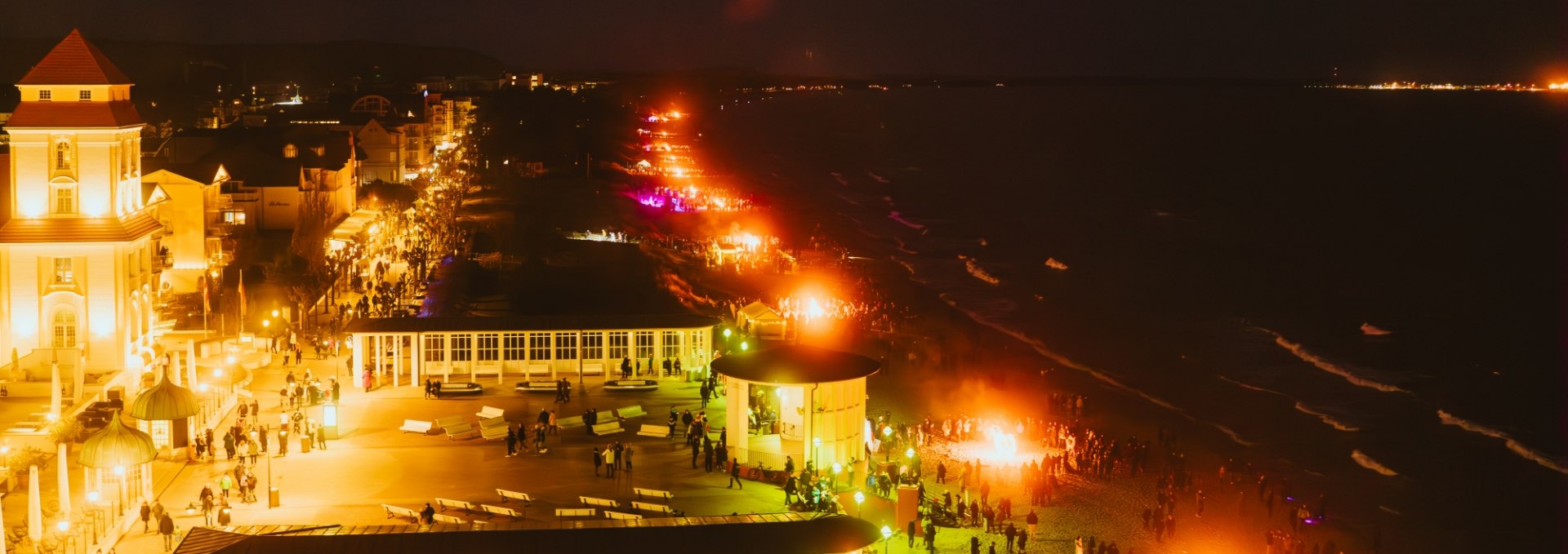 Nachtaufnahme der Osterfeuermeile in Binz mit beleuchteter Strandpromenade und Feuerstellen.