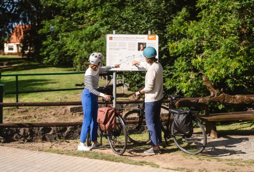 Zwei Radfahrer stehen am Schild zur Route der Norddeutschen Romantik // An zentralen Orten der Route finden Frauke und Wolf Informationen zu den Malern und der Region. // © MV-T/Gross Zwei Radfahrer stehen am Schild zur Route der Norddeutschen Romantik