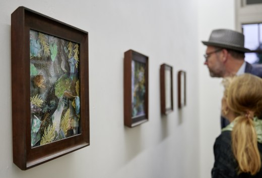 Besucher betrachten w&auml;hrend der Veranstaltungsreihe KUNST HEUTE gerahmte Naturcollagen in einer hellen Ausstellung.
