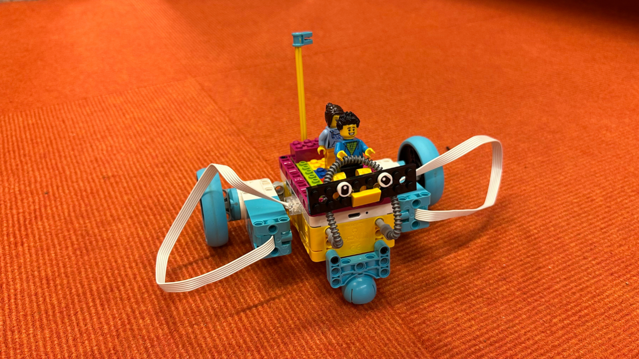 een kleine Lego robot met twee Lego figuren erop, oranje achtergrond // &copy; Stadtbibliothek Stralsund