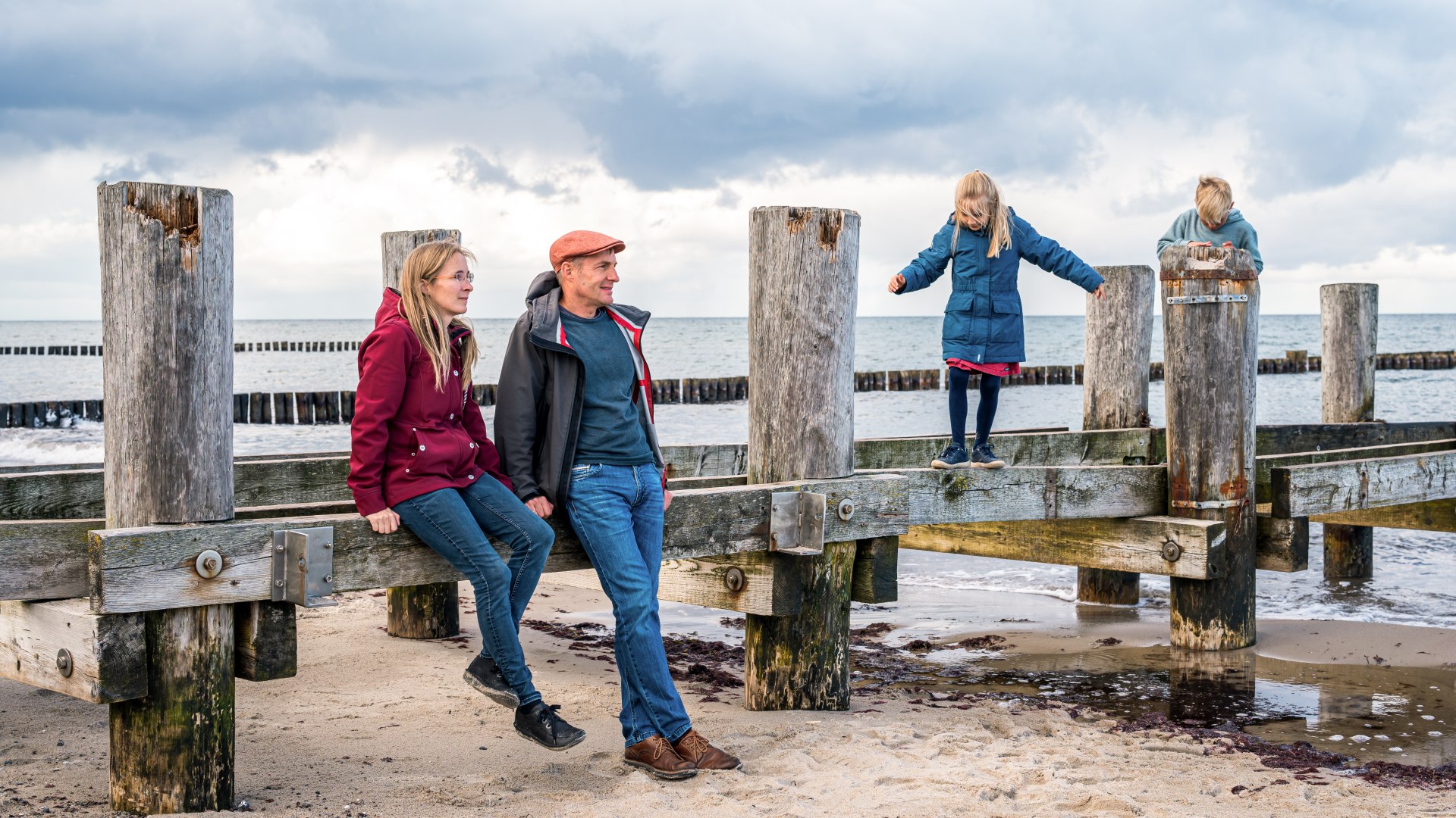 Familie an einem alten Holzgerüst für eine Seebrücke am Strand von Kühlungsborn - die Kinder turnen darauf rum. // Bei Wind und Wetter draußen: Familienurlaub an der Ostsee – hier in Kühlungsborn // © MV-T/Tiemann Familie an einem alten Holzgerüst für eine Seebrücke am Strand von Kühlungsborn - die Kinder turnen darauf rum.