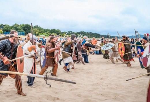 Die „Strand-Schlachten“ zwischen den Sippen gehören zu den Höhepunkten des Göhrener Wikingerfests, © TMV/Tiemann Als Wikinger verkleidete Personen laufen auf einander zu am Strand von Göhren