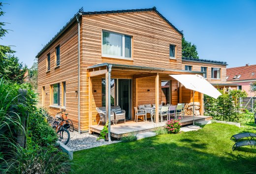 Ein Ferienhaus mit Holzverkleidung und etwas gr&uuml;ner Wiese davor.