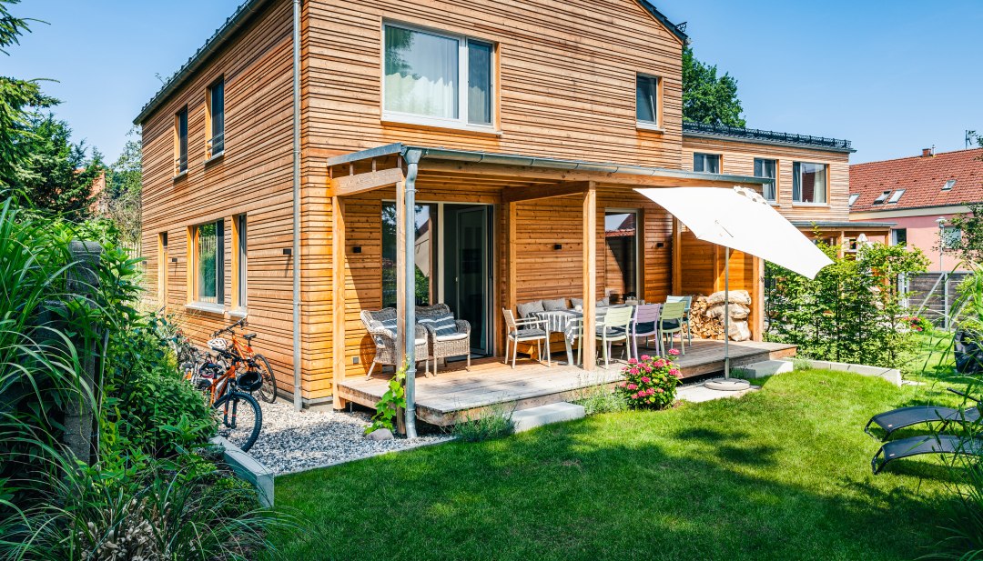 Ein Ferienhaus mit Holzverkleidung und etwas gr&uuml;ner Wiese davor.