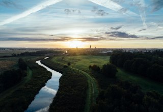 Sonnenaufgang &uuml;ber der Hansestadt Greifswald: Ein stiller Fluss schl&auml;ngelt sich durch Wiesen, w&auml;hrend Kircht&uuml;rme am Horizont langsam im Morgenlicht sichtbar werden. Mecklenburg-Vorpommern erwacht leise. // &copy; MV-T/G&auml;nsicke