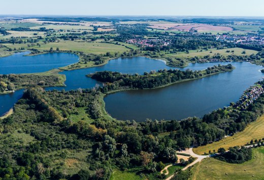 Luftaufnahme vom Teterower See mit Burgwallinsel, gr&uuml;nen Ufern, Feldern und Teterow im Hintergrund.