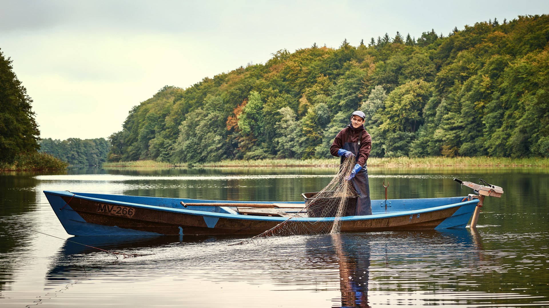 Fischer in der Mecklenburgischen Seenplatte zieht gerade seine Netze ein auf das Boot.