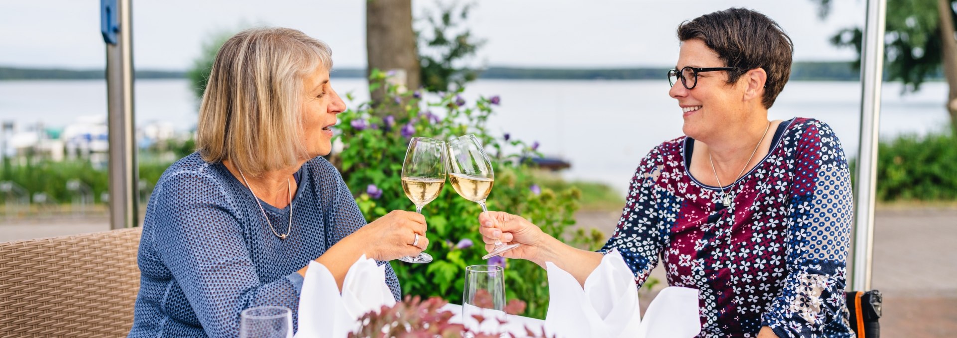 Es wird angesto&szlig;en an einem Tisch mit zwei Frauen und jeweils einem Sektglas.