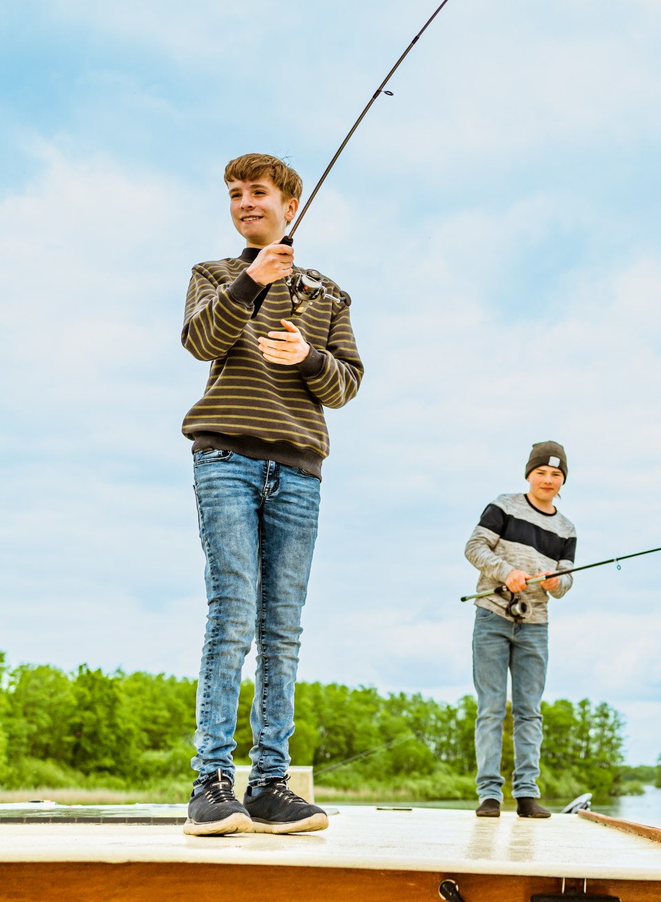 Twee kinderen vissen vanaf het dak van een woonboot in de zon.