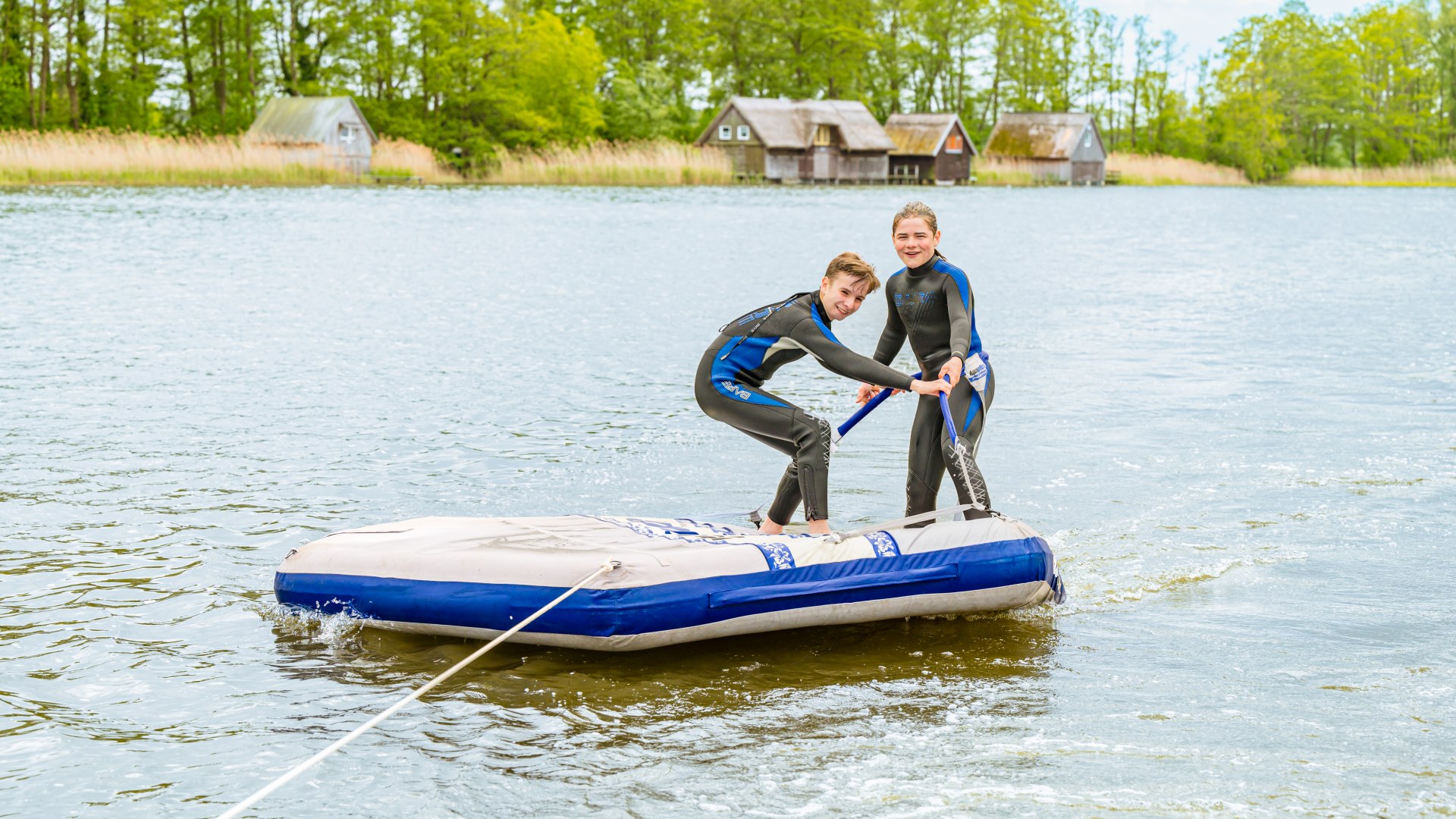 Zwei Kinder auf einer Badeinsel, die hinter einem Boot hinterher gezogen wird. // Auf der Badeinsel lassen sich Ferri und Theo über den See ziehen. Wer schafft es, länger stehen zu bleiben? // © MV-T/Tiemann Zwei Kinder auf einer Badeinsel, die hinter einem Boot hinterher gezogen wird.