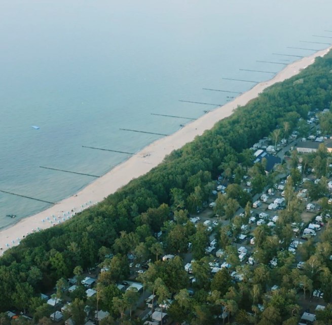 Luftaufnahme eines Campingplatzes an der Ostseeküste mit angrenzendem Sandstrand und Buhnen im Meer.