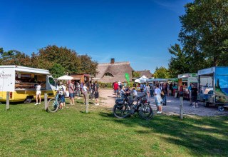 Der Ahrenshooper Sommerfrischemarkt lädt in entspannter Atmosphäre zum Stöbern und Genießen ein. Zwischen traditionellen reetgedeckten Häusern präsentieren regionale Händler an ihren Verkaufsanhängern ein vielfältiges Angebot – von frischen Backwaren bis hin zu Bio-Delikatessen. Das Bild zeigt das lebendige Treiben unter freiem Himmel, bei dem Besucher mit dem Fahrrad anreisen und an kleinen Tischen verweilen, um das typische Flair der Ostseeregion zu erleben. // © Fa. Voigt & Kranz UG, Prerow Der Ahrenshooper Sommerfrischemarkt lädt in entspannter Atmosphäre zum Stöbern und Genießen ein. Zwischen traditionellen reetgedeckten Häusern präsentieren regionale Händler an ihren Verkaufsanhängern ein vielfältiges Angebot – von frischen Backwaren bis hin zu Bio-Delikatessen. Das Bild zeigt das lebendige Treiben unter freiem Himmel, bei dem Besucher mit dem Fahrrad anreisen und an kleinen Tischen verweilen, um das typische Flair der Ostseeregion zu erleben. // © Fa. Voigt & Kranz UG, Prerow