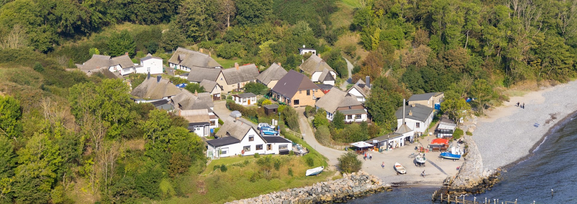 Luftaufnahme des Fischerdorfs Vitt auf der Insel R&uuml;gen. Zu sehen sind reetgedeckte H&auml;user, gr&uuml;ne Wiesen im Hintergrund und die Ostseek&uuml;ste mit einem kleinen Hafenbereich im Vordergrund.