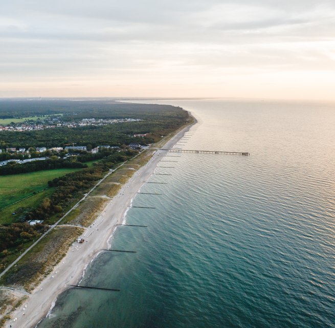 Luchtfoto van de pier en het strand van Graal-M&uuml;ritz, omgeven door bossen en weilanden, met de Baltische Zee in het licht van een sfeervolle zonsondergang.