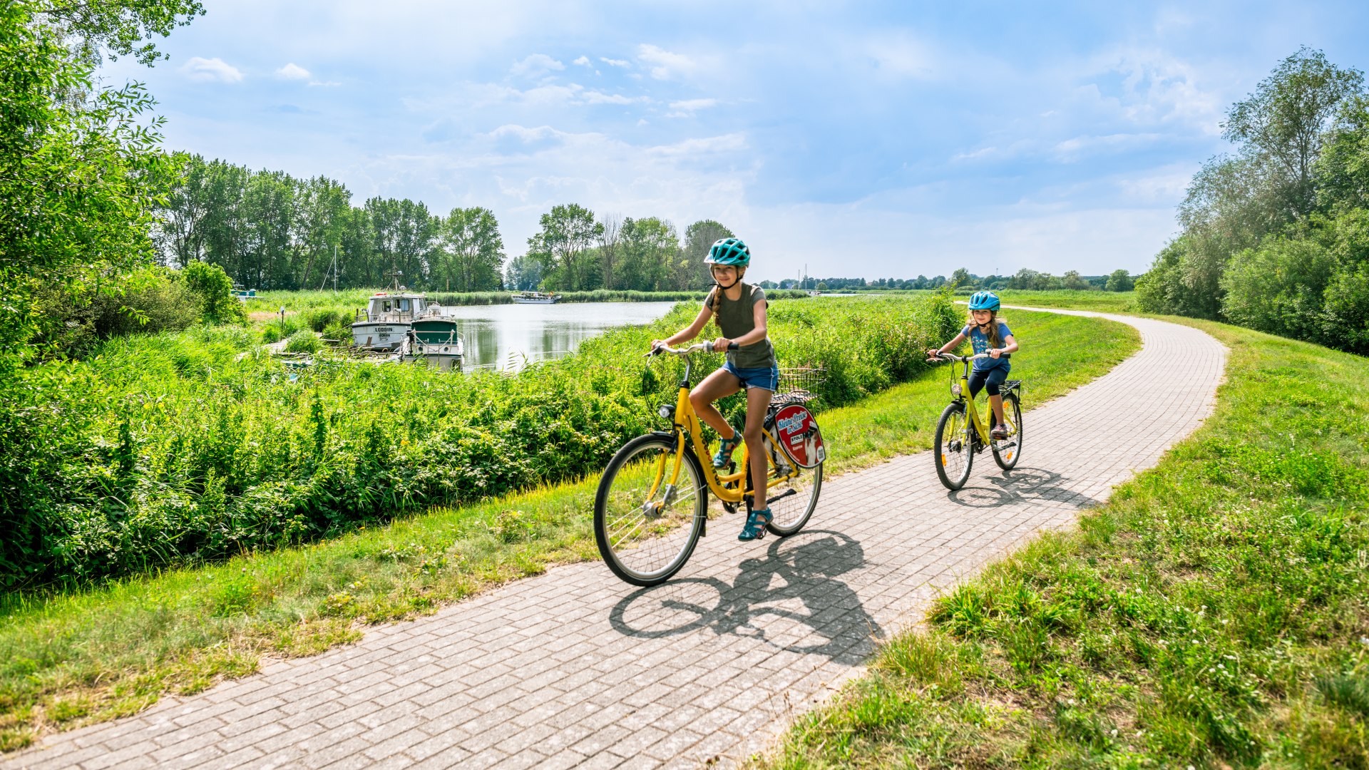 Zwei Kinder fahren entlang dem Achterwasser auf gelben Fahrrädern // Am Achterwasser kann man auch radeln. // © MV-T/Tiemann Zwei Kinder fahren entlang dem Achterwasser auf gelben Fahrrädern
