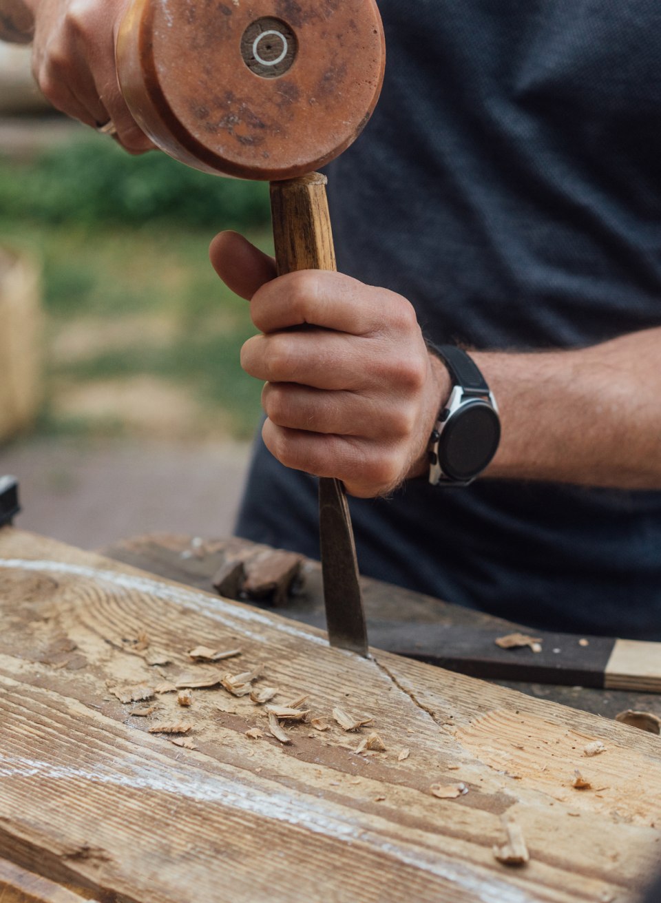 Eine Person formt beim Bildhauer-Workshop mit Kl&ouml;ppel und Mei&szlig;el etwas in ein gro&szlig;es St&uuml;ck Holz