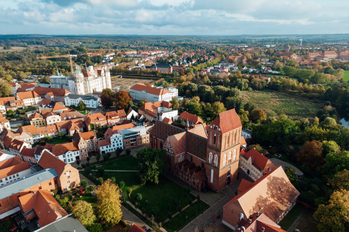 Baksteenarchitectuur ontmoet renaissancepracht: kasteel G&uuml;strow en de kathedraal kenmerken de historische oude stad. Tussen herfstkleurige bomen en rode daken zie je in vogelvlucht de eeuwenoude architectuur van Mecklenburg. Een wandeling door de steegjes leidt naar verborgen pleinen en architectonische schatten. // &copy; MV-T/Petermann