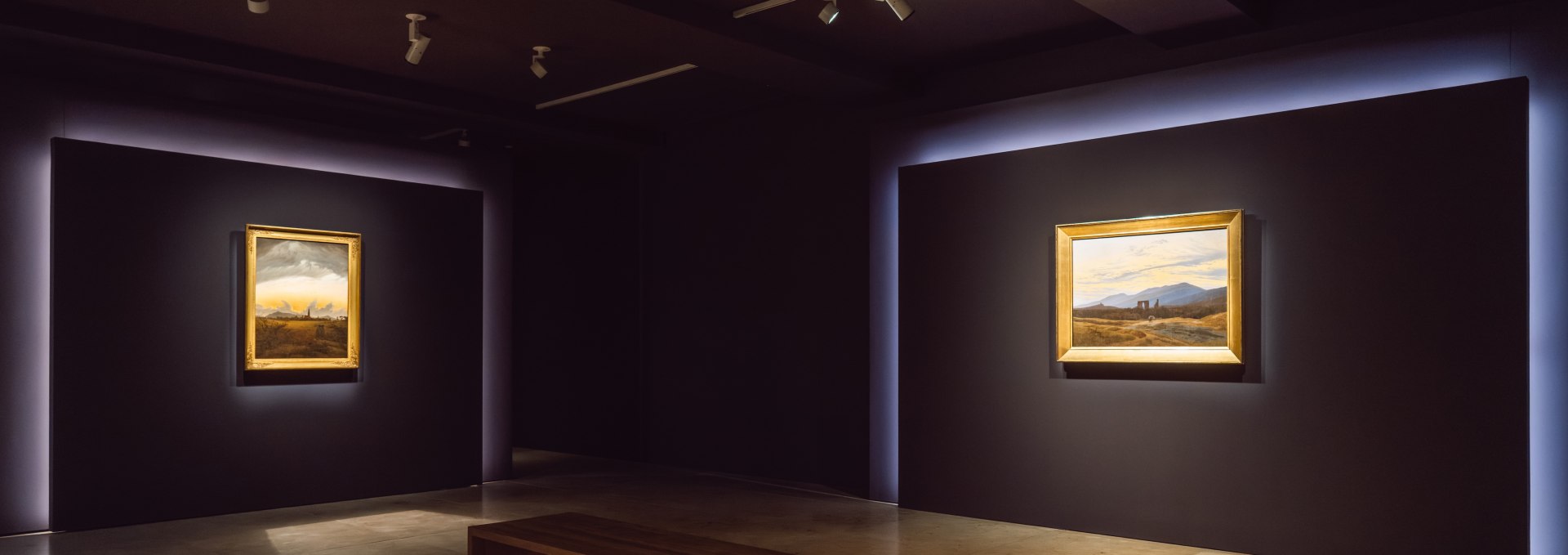 Zwei beleuchtete Landschaftsgemälde in minimalistischem Ausstellungsraum im Pommerschen Landesmuseum Greifswald. // Im Pommerschen Landesmuseum Greifswald inszeniert die Ausstellung Caspar David Friedrichs Landschaften wie Bühnenbilder. Die reduzierte Präsentation lenkt den Blick auf das Wesentliche – auf Licht, Weite und die Stille der Natur. Ein Raum, der zur Kontemplation einlädt. // © MV-T/Gross Zwei beleuchtete Landschaftsgemälde in minimalistischem Ausstellungsraum im Pommerschen Landesmuseum Greifswald.