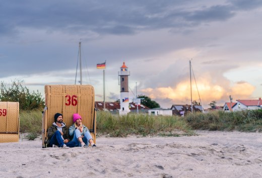 Paar sitzt im Strandkorb am Strand von Timmendorf auf Poel mit Blick auf Leuchtturm und Abendhimmel.