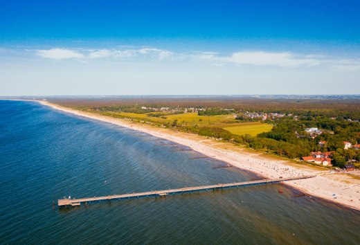 Luftaufnahme der Ostseeküste von Graal-Müritz mit Seebrücke, Sandstrand und Küstenwald. // Die Seebrücke ragt ins türkisblaue Wasser, der Sandstrand zieht sich kilometerweit entlang der Küste. Graal-Müritz lädt zum Baden, Spazieren und Durchatmen ein – zwischen Ostsee und grünen Wäldern liegt der Freiraum für Urlaubsmomente. // © MV-T/Friedrich Luftaufnahme der Ostseeküste von Graal-Müritz mit Seebrücke, Sandstrand und Küstenwald.