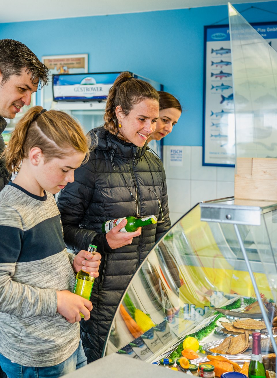 Zwei Familien stehen am Tresen vom Fischerhof Vipperow und suchen sich ein Fischbrötchen aus. // Bismarckhering, Hecht und Backfisch im Brötchen, bitte: Beim Fischerhof in Vipperow sind die beiden Familien schon Stammgäste. // © MV-T/Tiemann Zwei Familien stehen am Tresen vom Fischerhof Vipperow und suchen sich ein Fischbrötchen aus.