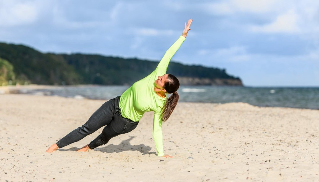 Der seitliche Stütz mit Armheben spricht die Muskulatur im gesamten Körper an., © TMV/Tiemann Der seitliche Stütz im Sand mit Armheben spricht die Muskulatur im gesamten Körper an.
