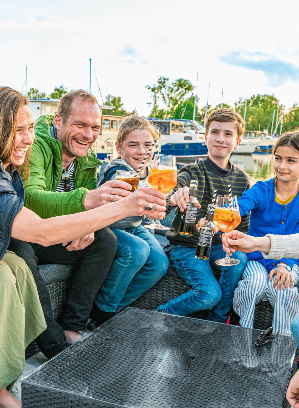 Zwei Familien stoßen mit Getränken an in der Pirate`s Bar. // Schöner Ausklang in der Pirate’s Bar: Mit den Füßen im Sand stoßen die beiden befreundeten Familien auf den tollen Urlaub an. // © MV-T/Tiemann Zwei Familien stoßen mit Getränken an in der Pirate`s Bar.