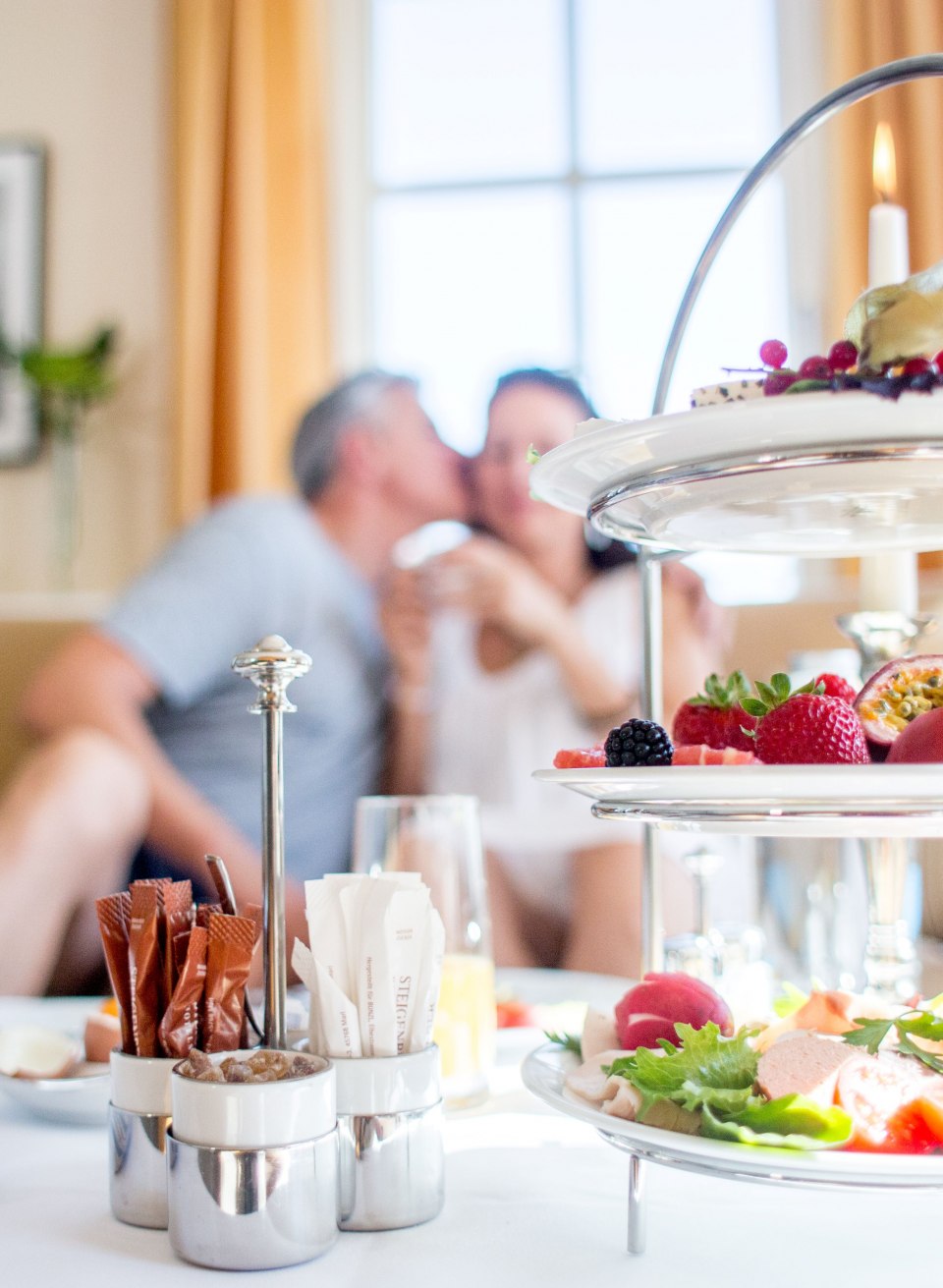 Fr&uuml;hst&uuml;ck mit frischen Br&ouml;tchen, Obst und Aufschnitt vor einem Paar beim Kuss im Ostseebad Heringsdorf.