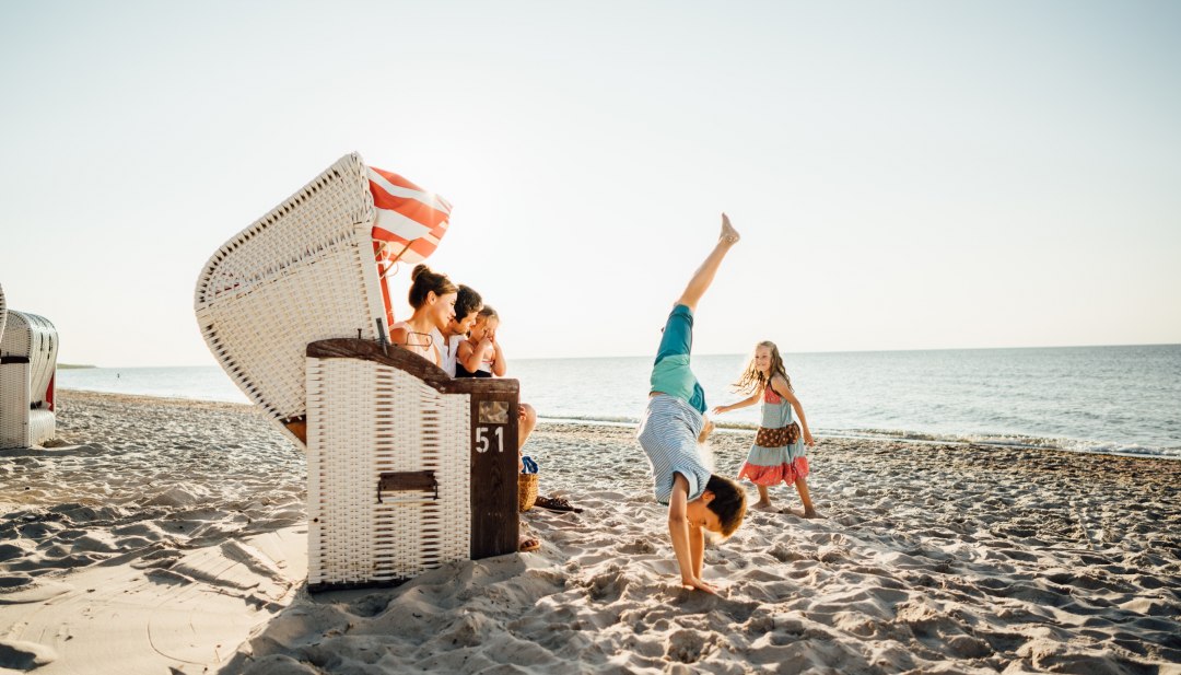 Familie am Ostseestrand Dierhagen mit Strandkorb, Kinder machen Handstand und spielen im Sand.