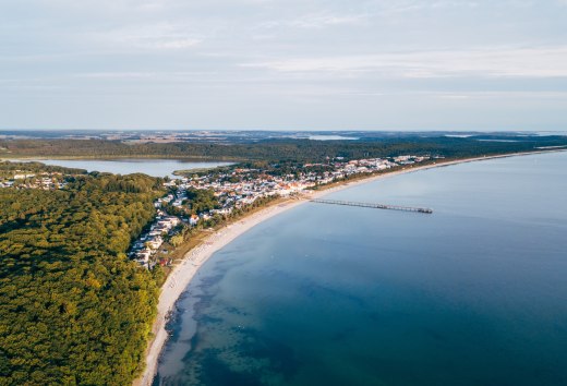 Luftaufnahme von Binz auf R&uuml;gen mit Seebr&uuml;cke, K&uuml;stenlinie und umliegenden W&auml;ldern.