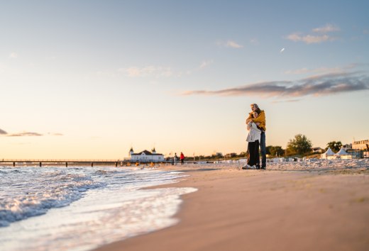 Ein Paar steht am Strand von Ahlbeck in Umarmung, die Seebr&uuml;cke und Abendhimmel im warmen Licht.