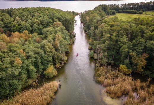 Ein Kanu paddelt durch einen kleinen Kanal von einem See in den anderen.