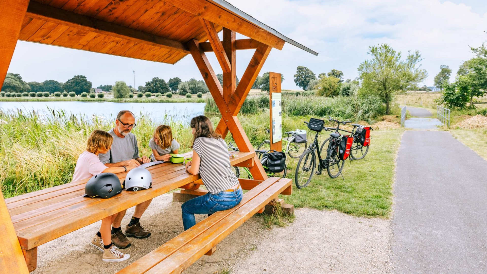 Eine Familie macht Pause auf einem Rastplatz neben einem See nach einer Fahrradtour. // Auch die fittesten Radfahrer brauchen mal Pause. Und im Hintergrund glitzert in Mecklenburg immer schon der nächste See. // © MV-T/Tiemann Eine Familie macht Pause auf einem Rastplatz neben einem See nach einer Fahrradtour.