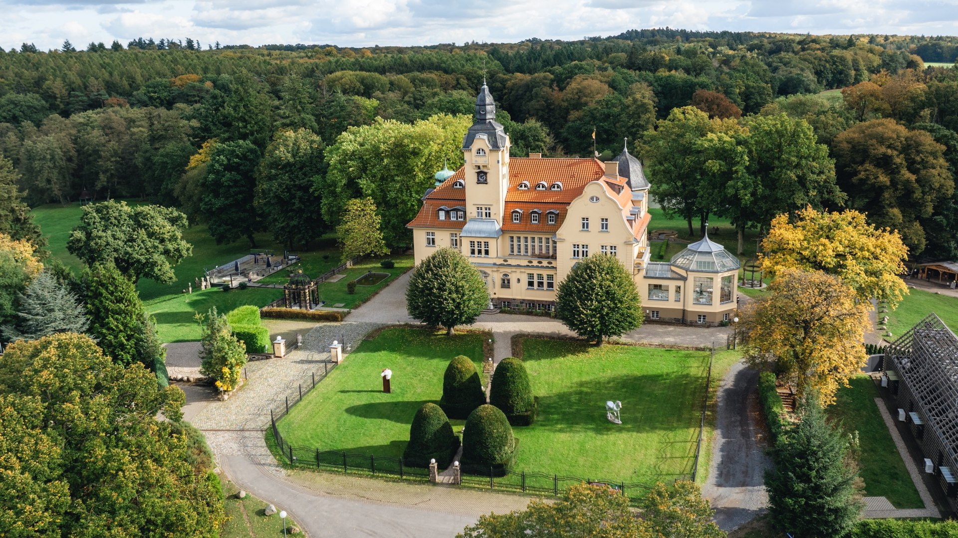 Luftaufnahme des Bernsteinschlosses Wendorf, umgeben von grünen Wiesen und Bäumen unter einem leicht bewölkten Himmel. // Majestätischer Blick – Das Bernsteinschloss Wendorf eingebettet in die grüne Landschaft. // © MV-T/Gross Luftaufnahme des Bernsteinschlosses Wendorf, umgeben von grünen Wiesen und Bäumen unter einem leicht bewölkten Himmel.
