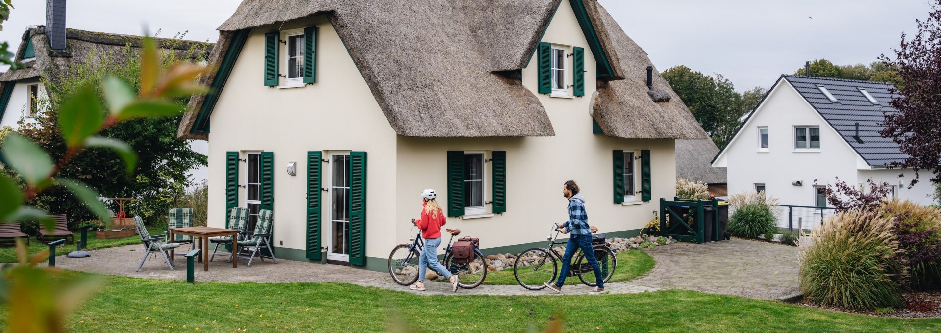 Ein Paar mit Fahrr&auml;dern vor einem charmanten Reetdach-Ferienhaus auf der Insel Poel.