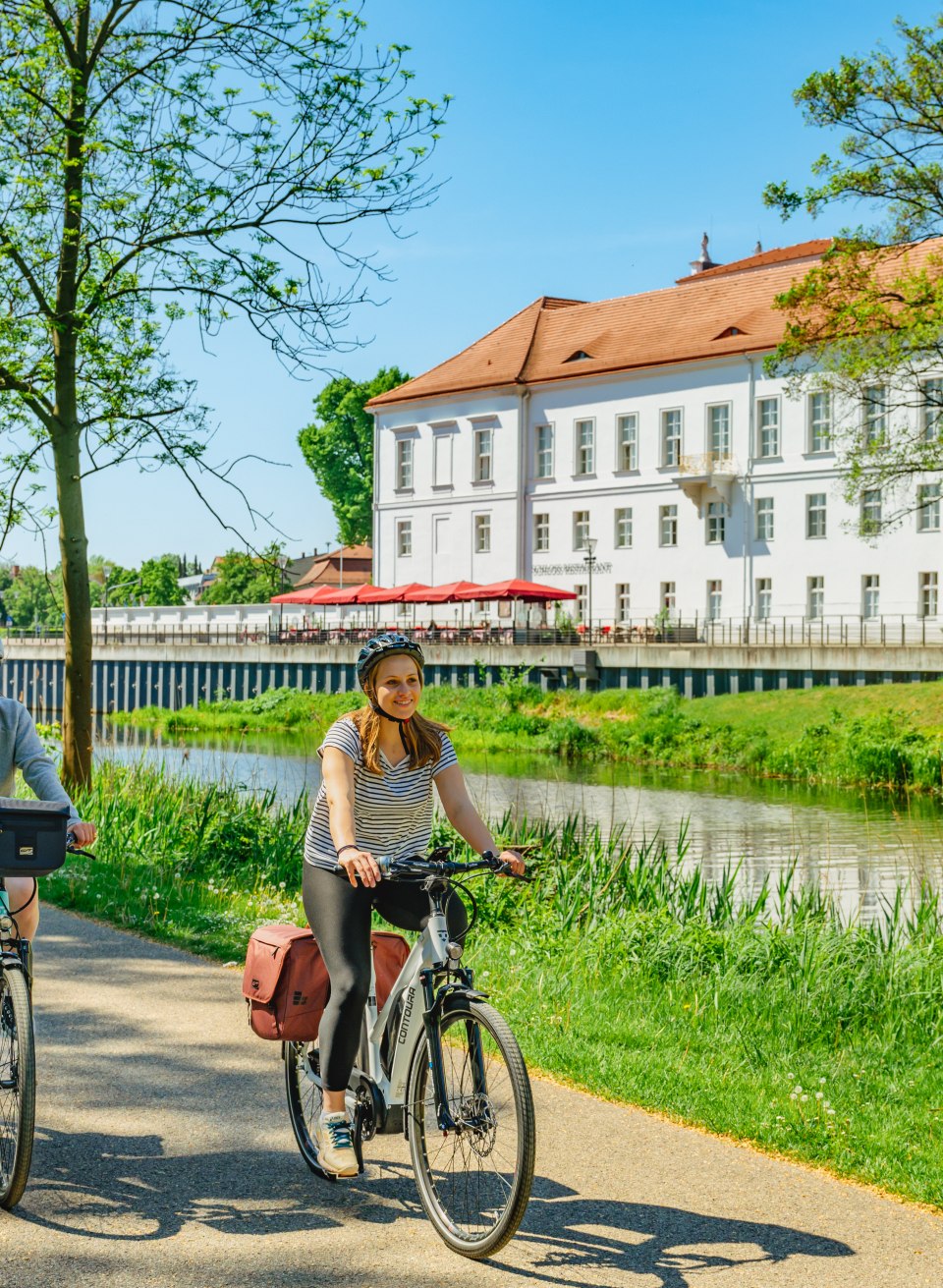 Mutter und Tochter fahren mit dem Rad am Schloss Oranienburg vorbei // In Oranienburg gibt’s ein Schloss und einen Radweg direkt am Wasser // © MV-T/Tiemann Mutter und Tochter fahren mit dem Rad am Schloss Oranienburg vorbei