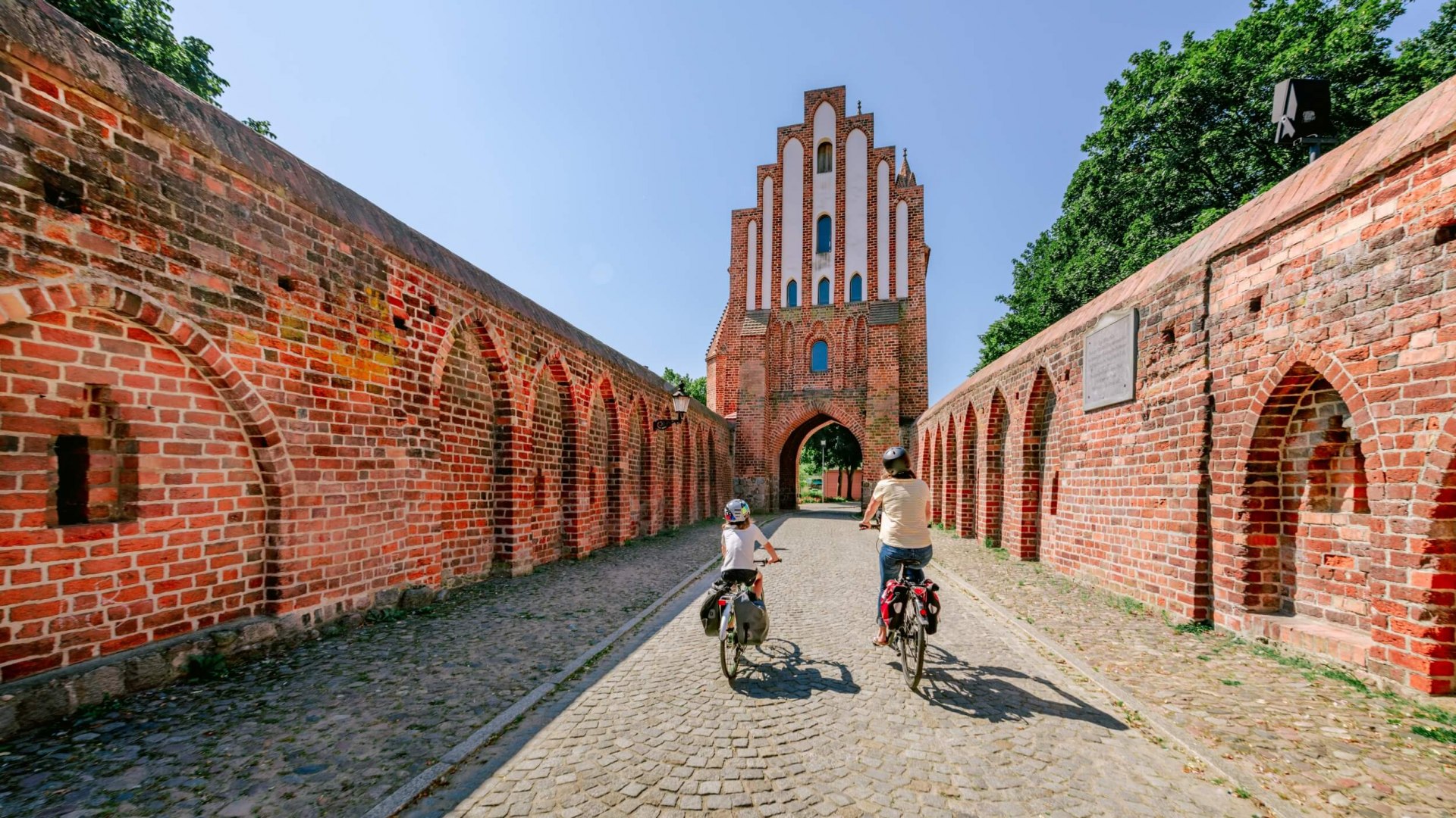 Eine Mutter mit Kind fährt mit dem Fahrrad durch das Friedländer Tor in Neubrandenburg. // Das Friedländer Tor in Neubrandenburg // © MV-T/Tiemann Eine Mutter mit Kind fährt mit dem Fahrrad durch das Friedländer Tor in Neubrandenburg.