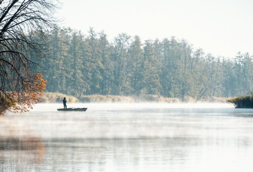 Angler im Boot auf der nebelverhangenen Peene im Herbst, umgeben von herbstlichen B&auml;umen.