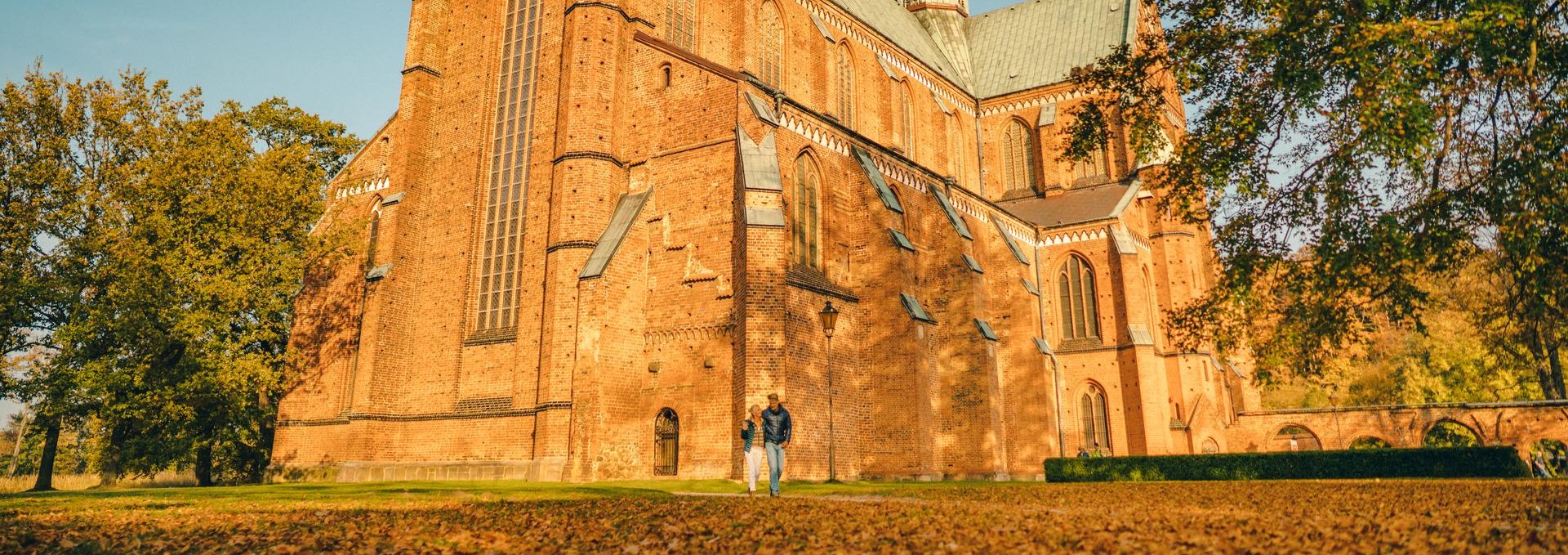 Een echtpaar wandelt voor de Bad Doberan Minster in de herfst. Bladeren liggen op de grond voor de kathedraal.