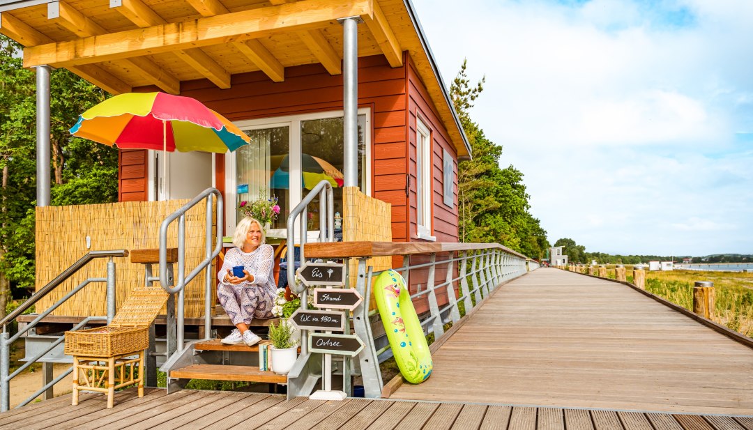 Een vrouw zit op de promenade bij haar kleine snackbar, waar ze ook strandstoelen verhuurt in Boltenhagen. // Het mooiste kantoor: Heike's strandstoel is een echte oase van gastvrijheid. Ze serveren ook lattes! // © MV-T/Tiemann Een vrouw zit op de promenade bij haar kleine snackbar, waar ze ook strandstoelen verhuurt in Boltenhagen.
